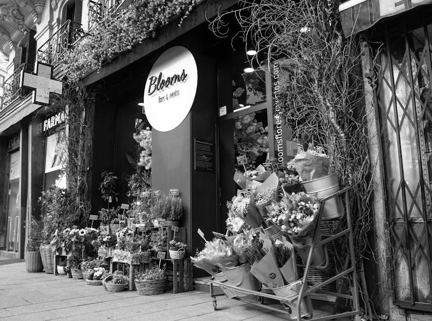 A black and white photograph of the storefront of Bloomz, a florist specializing in flowers and bouquets. The shop's exterior is decorated with an abundant display of fresh floral arrangements, includ