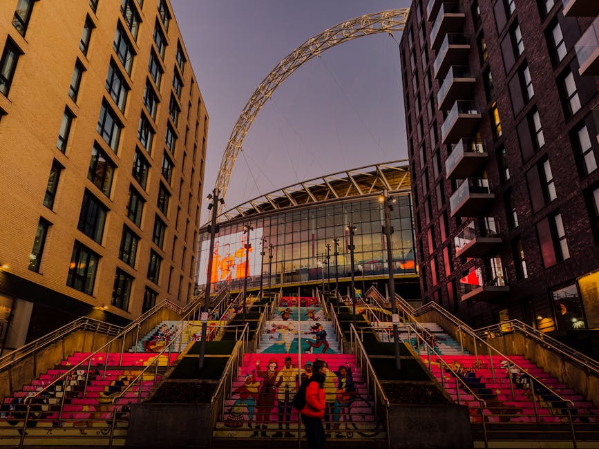 An outdoor floral arrangement featuring a bouquet of fresh flowers held by a person, set against a backdrop of urban stairs decorated with vibrant, colorful floral murals. The bouquet includes a mix o