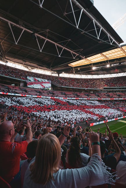 The image features a vibrant floral arrangement placed on a table inside a well-lit stadium during a match or event. The bouquet includes a mix of fresh flowers such as red roses, white lilies, and pi